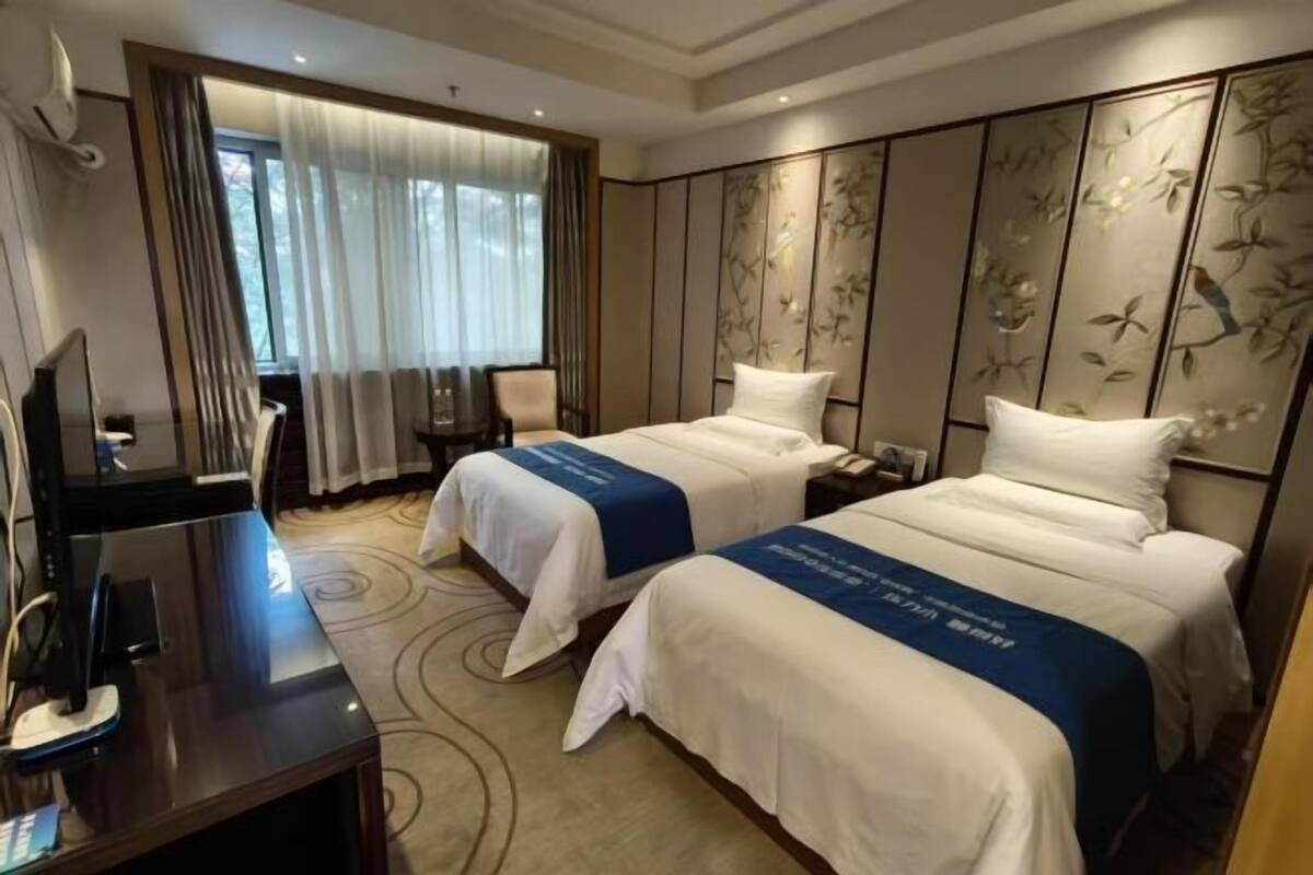 A hotel room with two beds, a desk, and a television.