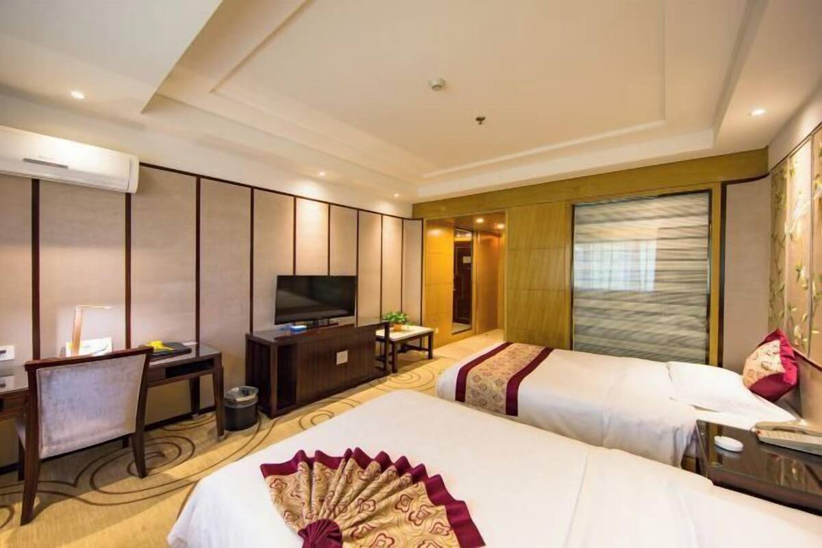 A hotel room with two beds, a desk with a chair, a television, and a large window.