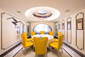 Een eetgedeelte met een ronde tafel, gele stoelen en een centrale kroonluchter.