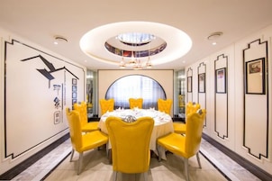 A dining area with a round table, yellow chairs, and a central chandelier.
