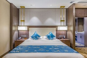 Habitación de hotel con una cama grande, dos mesitas de noche, un velador, cabecera con iluminación integrada y vista al baño.