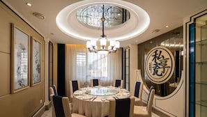 Une table de salle à manger ronde, entourée de chaises, un lustre et des œuvres d’art encadrées accrochées aux murs.