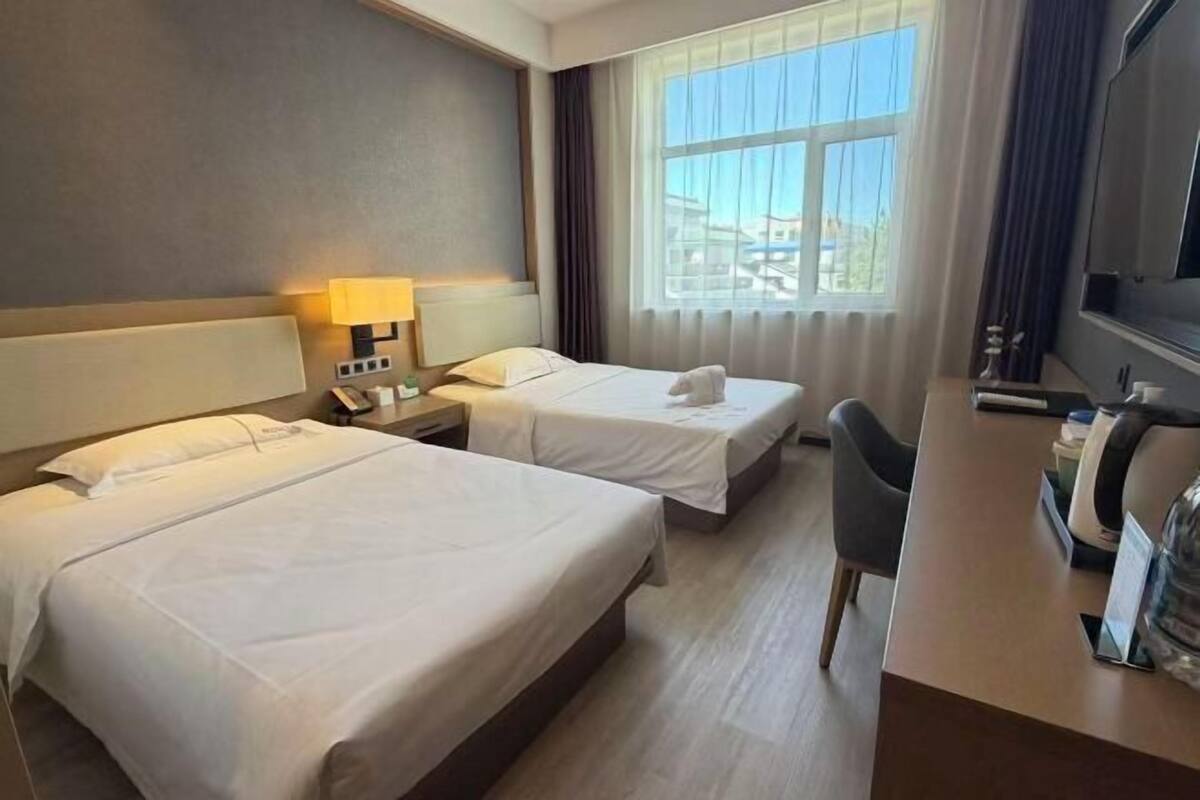 A hotel room with two beds, a desk, a chair, a TV, and a window with curtains.