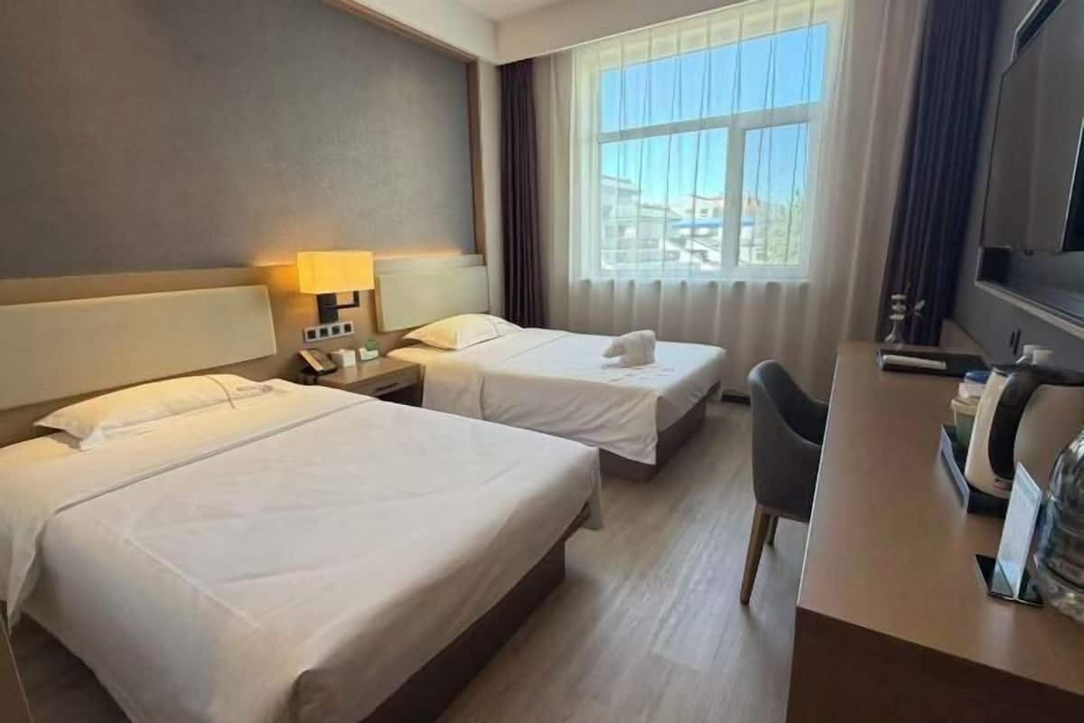 A hotel room with two beds, a desk, a chair, a TV, and a window with curtains.