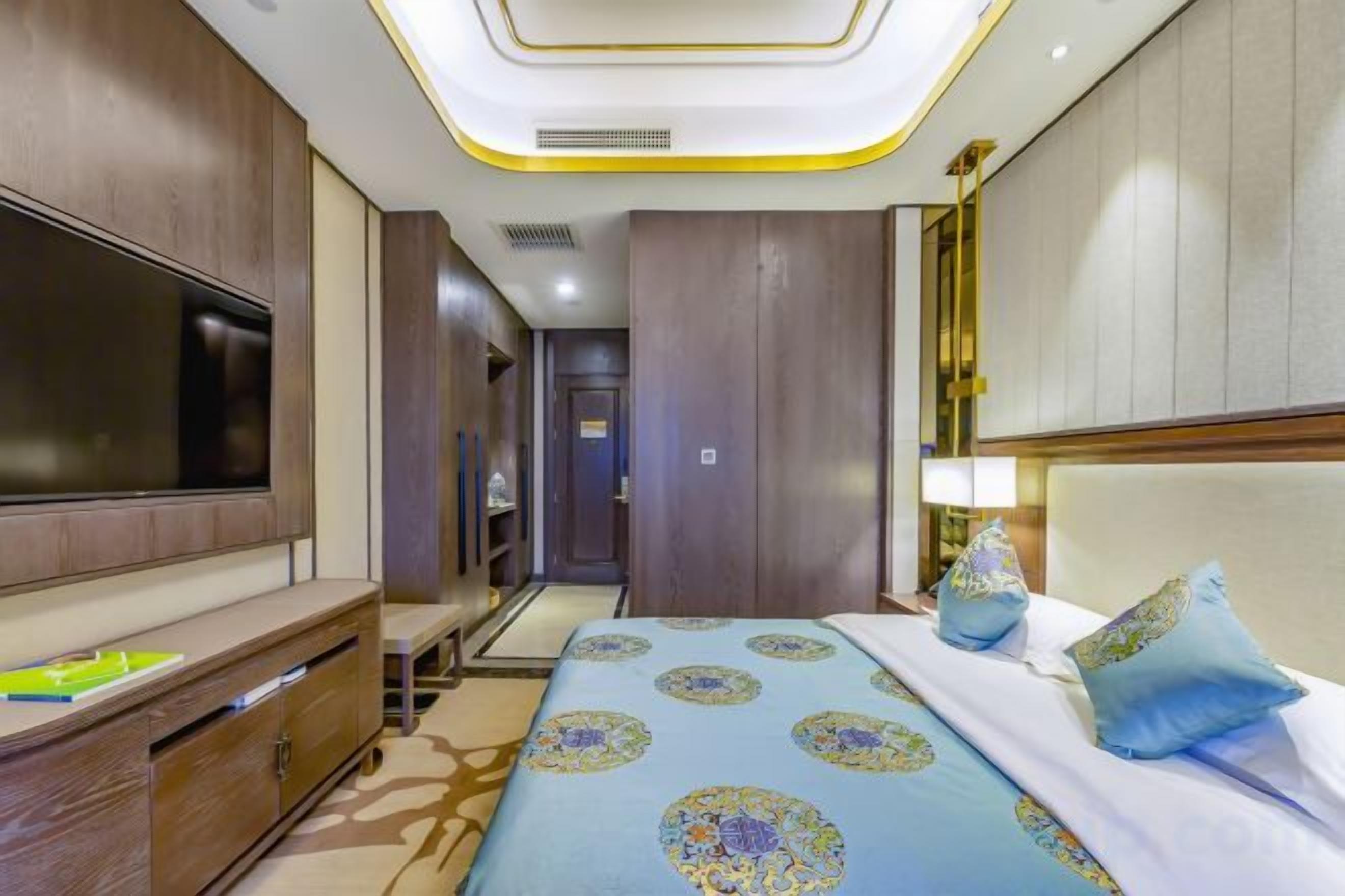 Quarto de hotel com televisão de tela plana grande, cama com roupa de cama estampada, mesa de cabeceira e abajur.