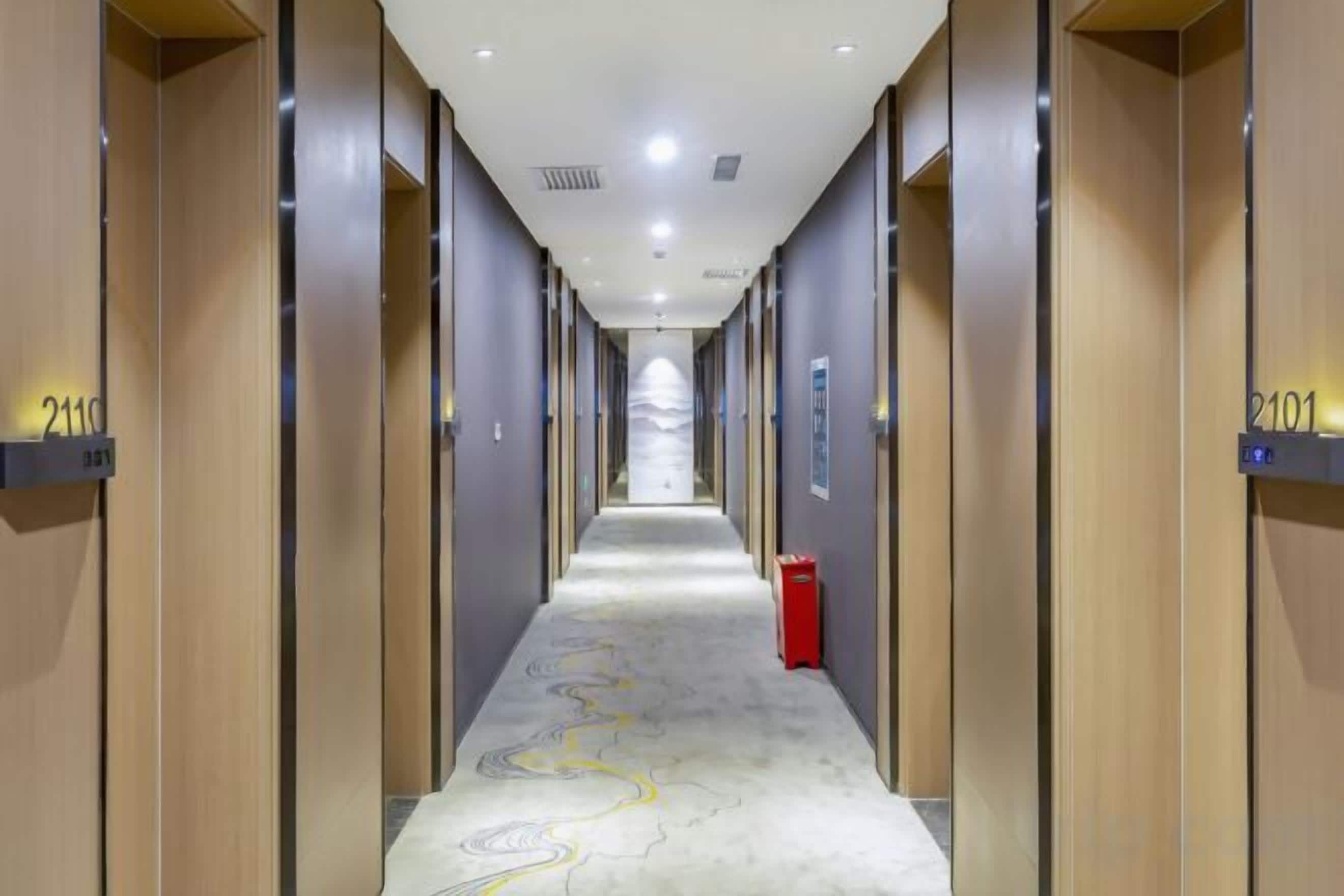 Pasillo de hotel con puertas numeradas 2119 y 2101, un extintor rojo y una alfombra estampada.