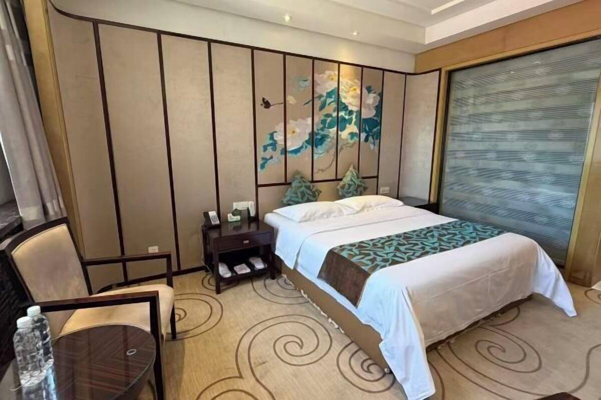 A hotel room with a bed, a desk, a chair, a nightstand, and a large window with a view.