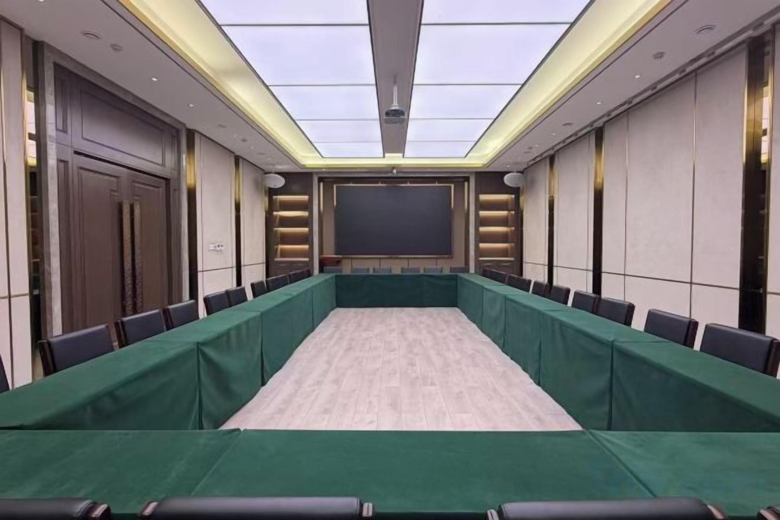 A conference room with a long table, chairs, a projector screen, and a ceiling with lights.
