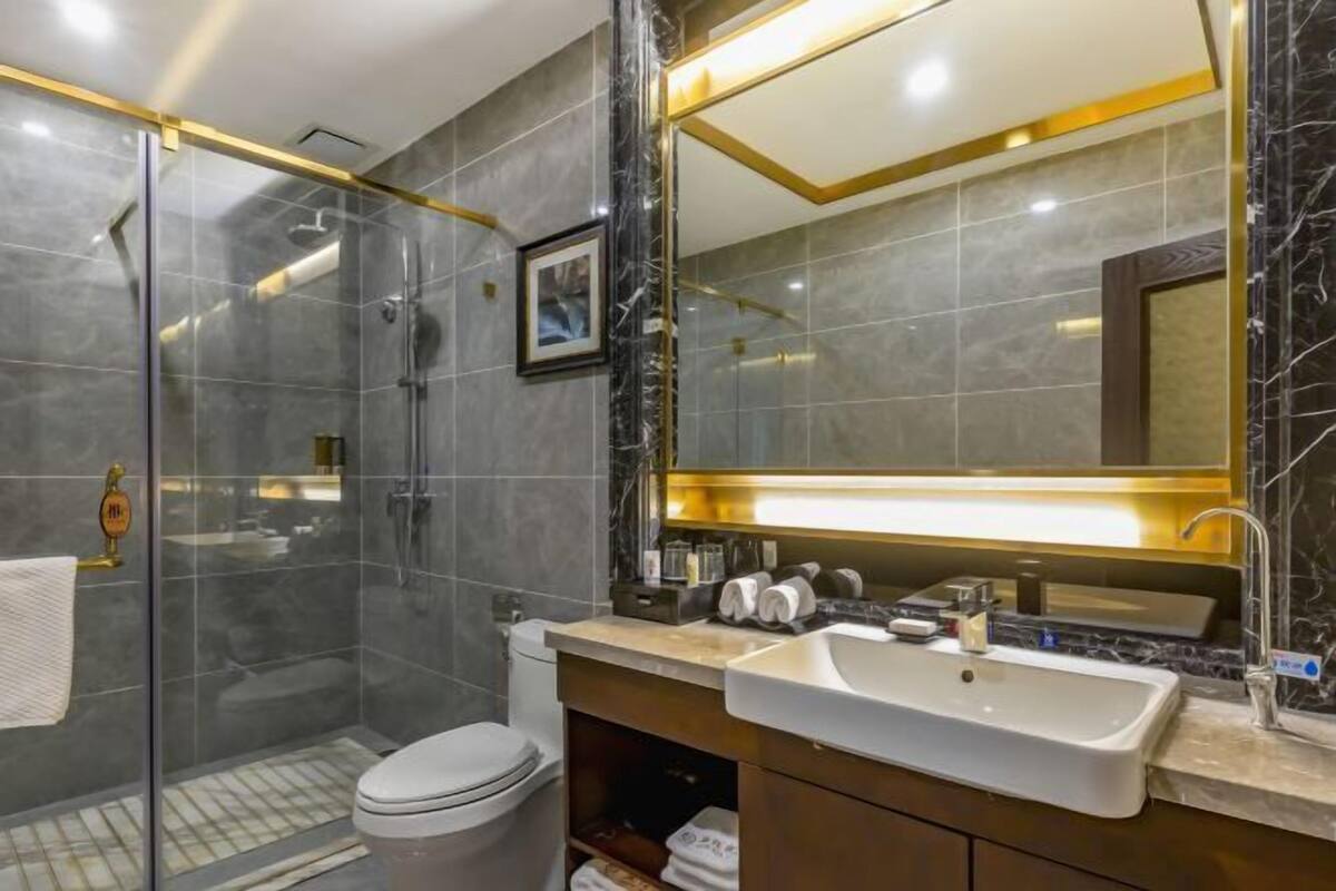 A modern bathroom with a glass-enclosed shower, a white toilet, a vanity with a sink, and a large mirror.