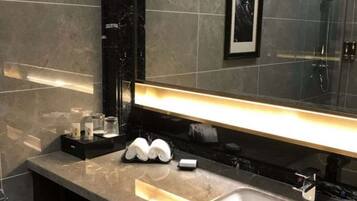 A modern bathroom with a marble countertop, a large mirror, and a shower area.