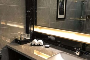 Un baño moderno con encimera de mármol, un espejo grande y zona de ducha.