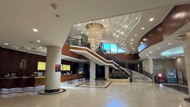 Un hall d’entrée spacieux avec un escalier central, un comptoir d’accueil et un lustre.