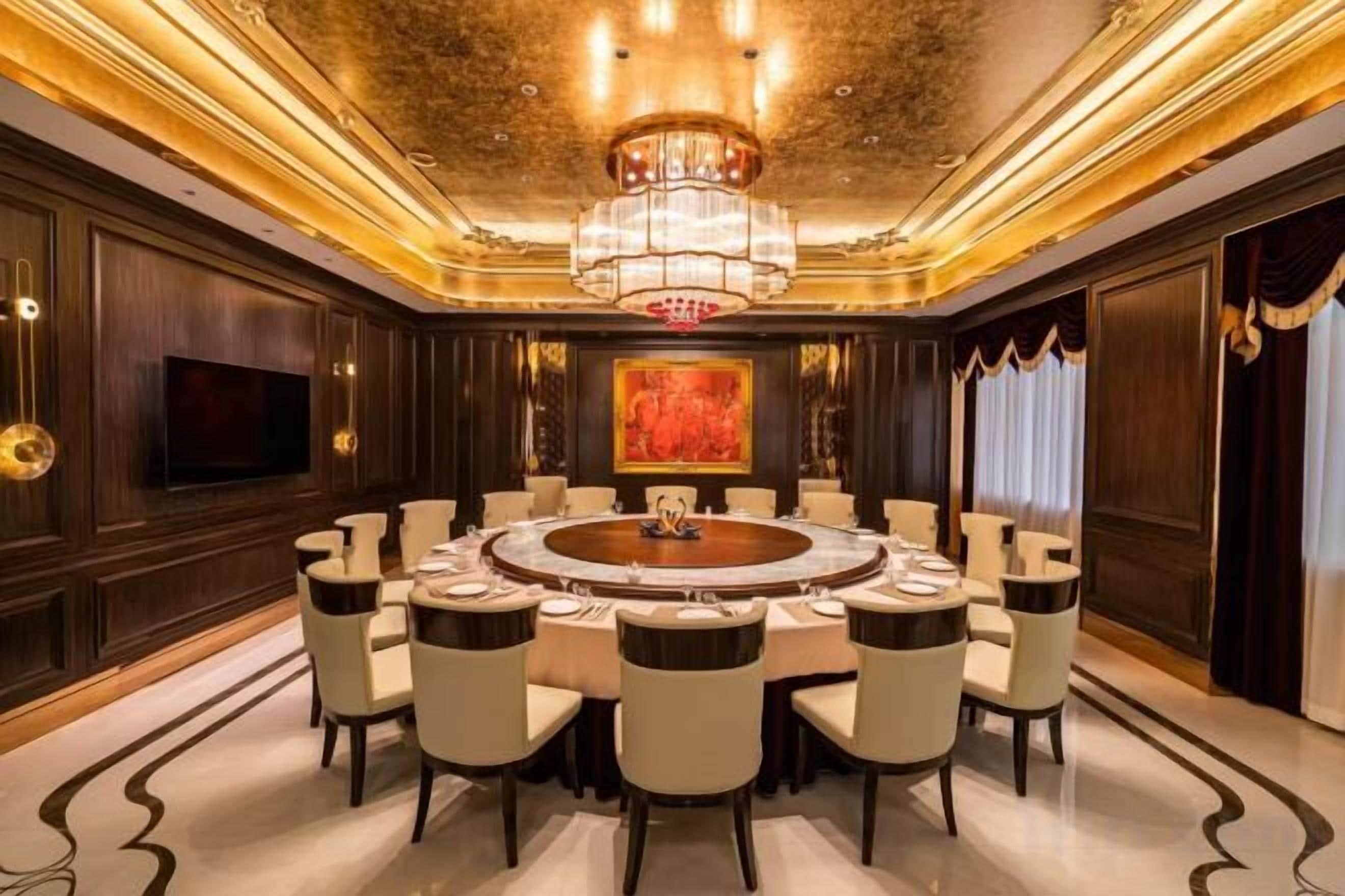 A luxurious dining room with a round table, multiple chairs, a chandelier, and a large painting on the wall.