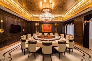 A luxurious dining room with a round table, multiple chairs, a chandelier, and a large painting on the wall.