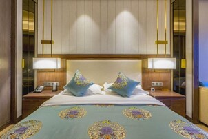 Una habitación de hotel con una cama grande, dos lámparas de noche, una mesita de noche y un cabecero de madera.