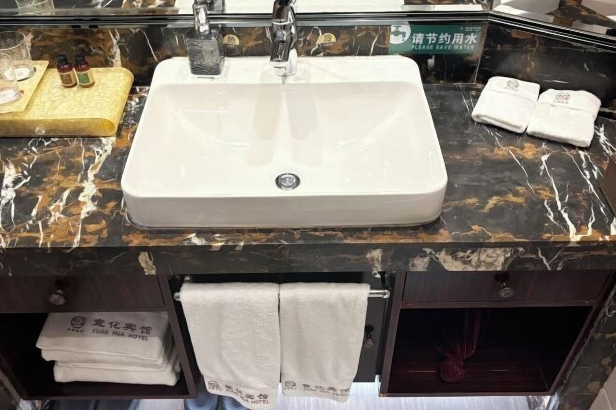 Un baño con un lavamanos blanco, un espejo y un perchero. Hay toallas colgadas en el perchero y una botella de champú en la encimera.