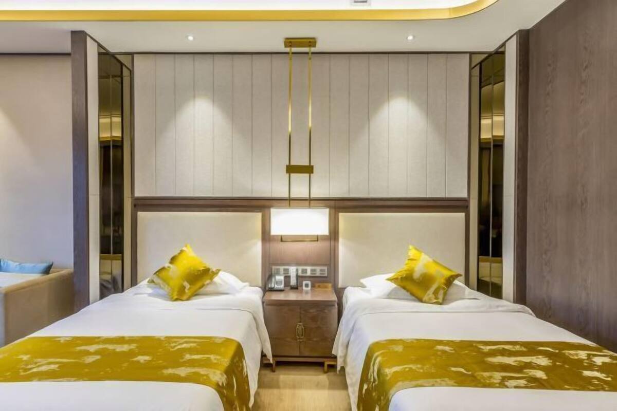 A hotel room with two beds, a nightstand, a lamp, and a mirror.