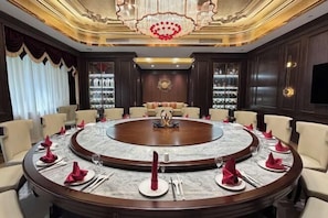 Une salle de conférence avec une table ronde au centre, entourée de chaises, et un lustre.
