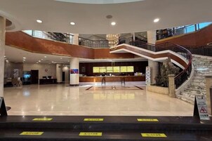 A spacious lobby with a reception desk, a staircase, and a high ceiling.