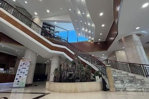Un vestíbulo de hotel con una escalera central, varios niveles y una recepción.