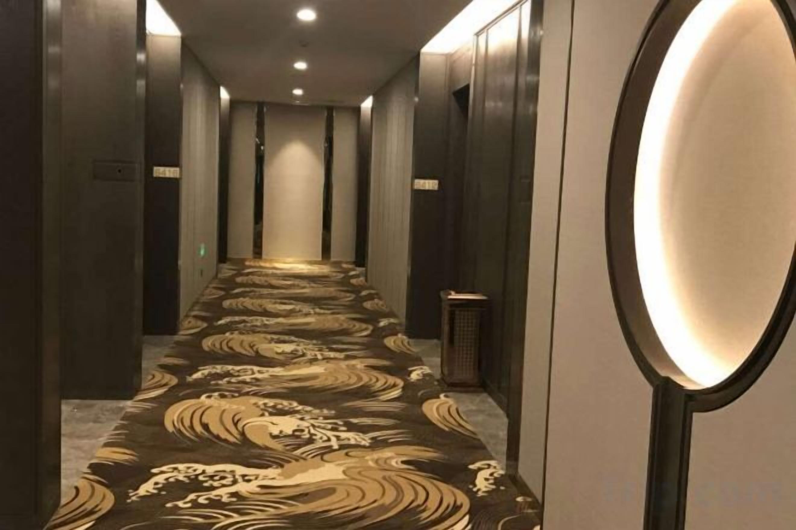 Corredor de hotel com carpete estampado, espelho e lixeira.