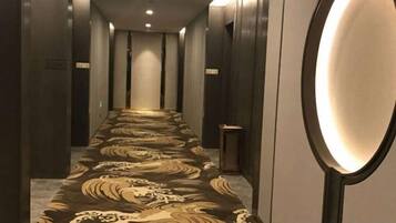 Corredor de hotel com carpete estampado, espelho e lixeira.