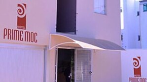A multi-story building with a prominent vertical black column, multiple windows, and air conditioning units. The building has a sign with the logo and name "Prime MOC". - Prime Moc Hotel (Montes Claros)
