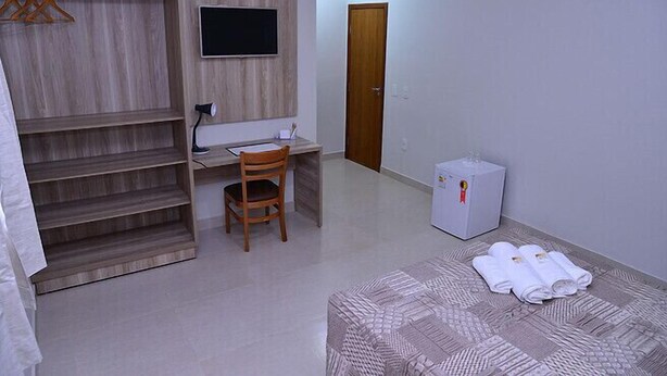 A bedroom with a bed, a desk, a chair, a wardrobe, a TV, and a door. - Prime Moc Hotel (Montes Claros)
