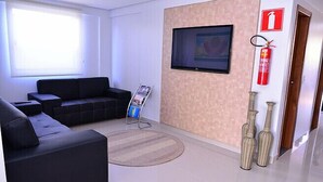 A modern living room with a black sofa, a flat-screen TV mounted on the wall, a fire extinguisher, and decorative vases. - Prime Moc Hotel (Montes Claros)