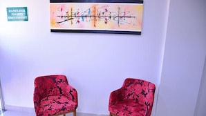 Two red floral armchairs with wooden legs in a room with a white wall and a colorful abstract painting above them. - Prime Moc Hotel (Montes Claros)
