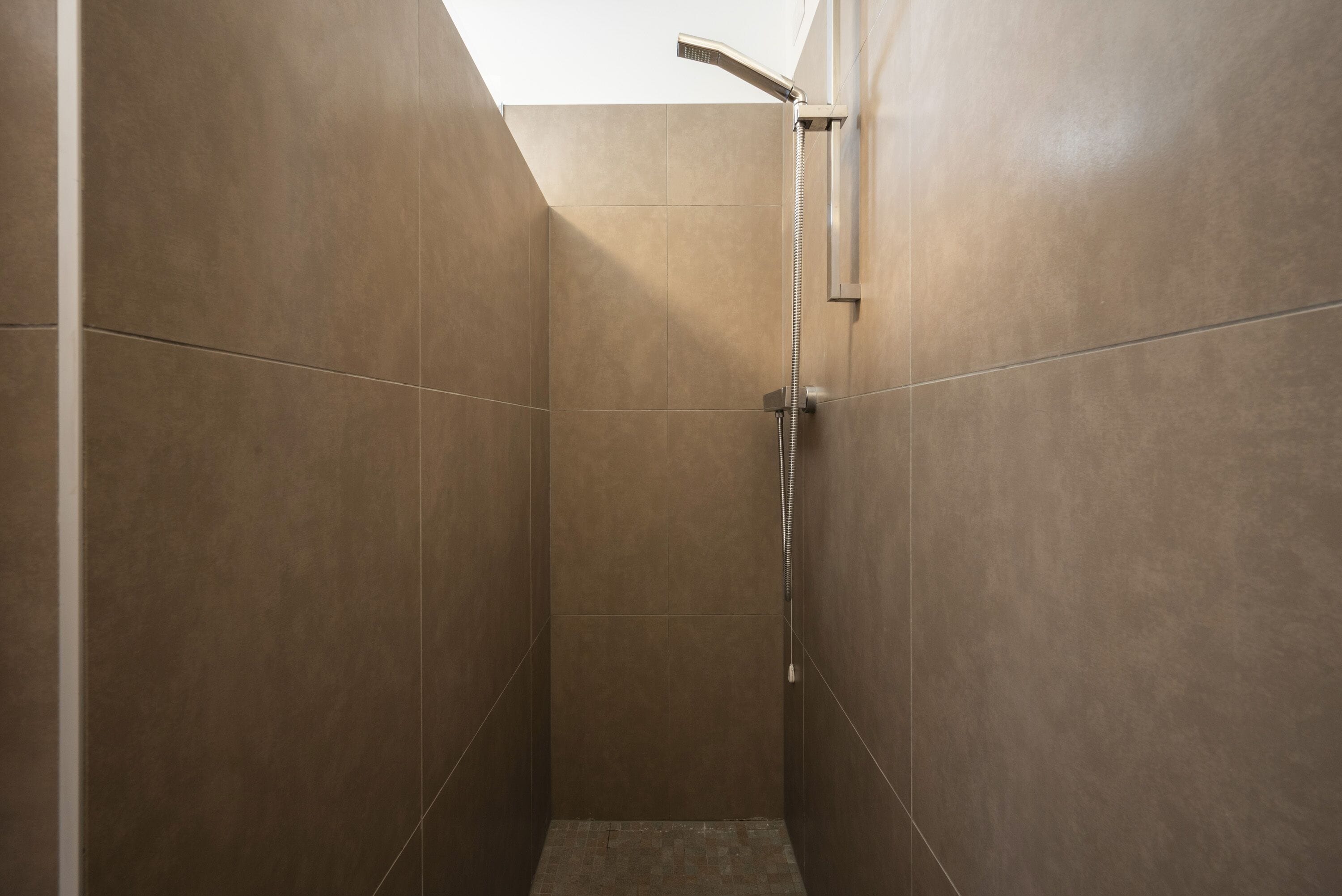 A modern shower with a handheld showerhead, tiled walls, and a sloped ceiling.