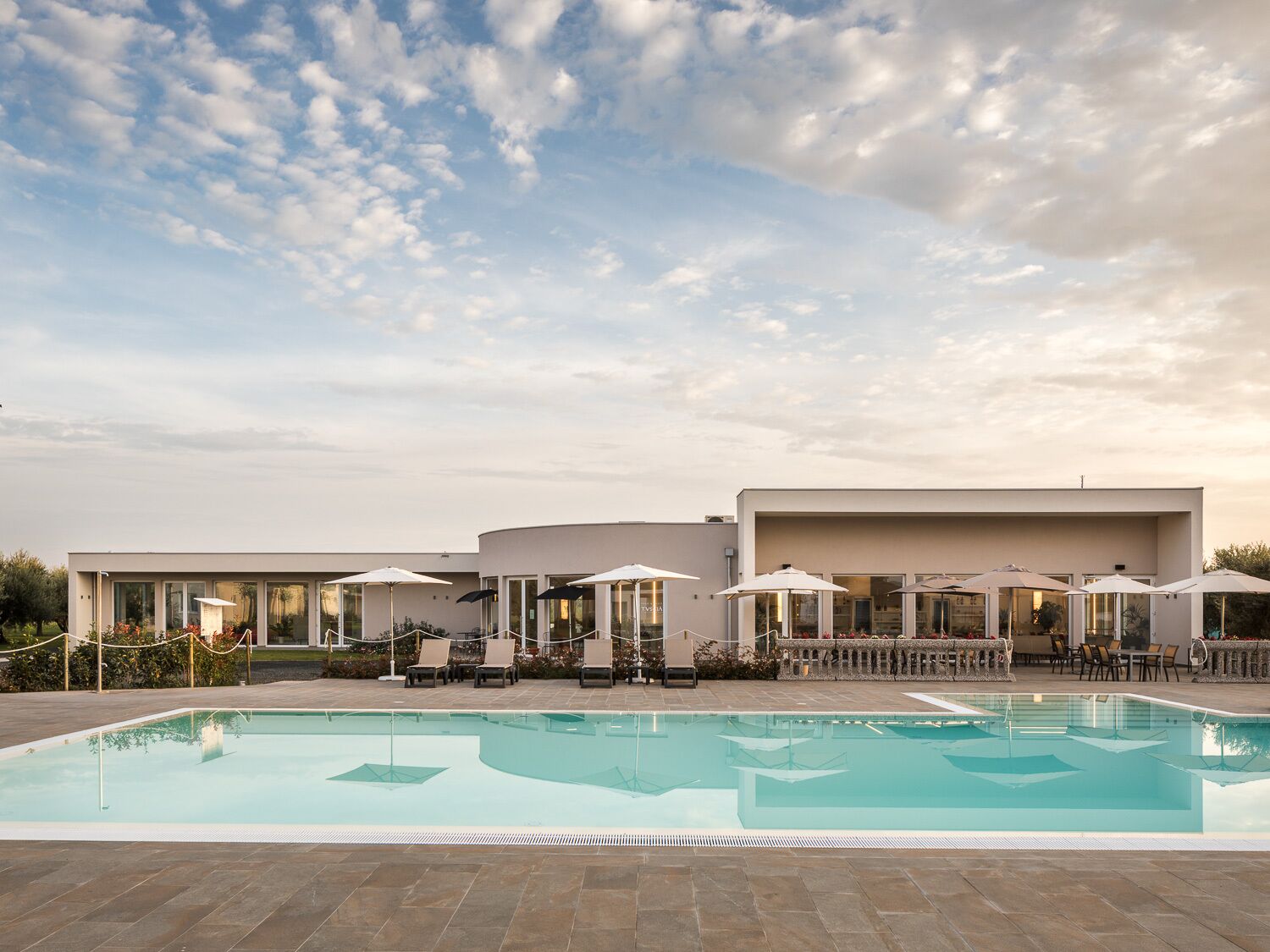 Un hotel moderno con piscina, zona de estar al aire libre y cielo despejado.