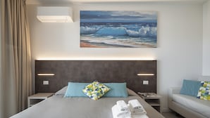 Ein modernes Hotelzimmer mit einem großen Bett, einem Kopfteil mit integrierter Beleuchtung, einem Meeresbild und ordentlich gefalteten Handtüchern auf dem Bett.