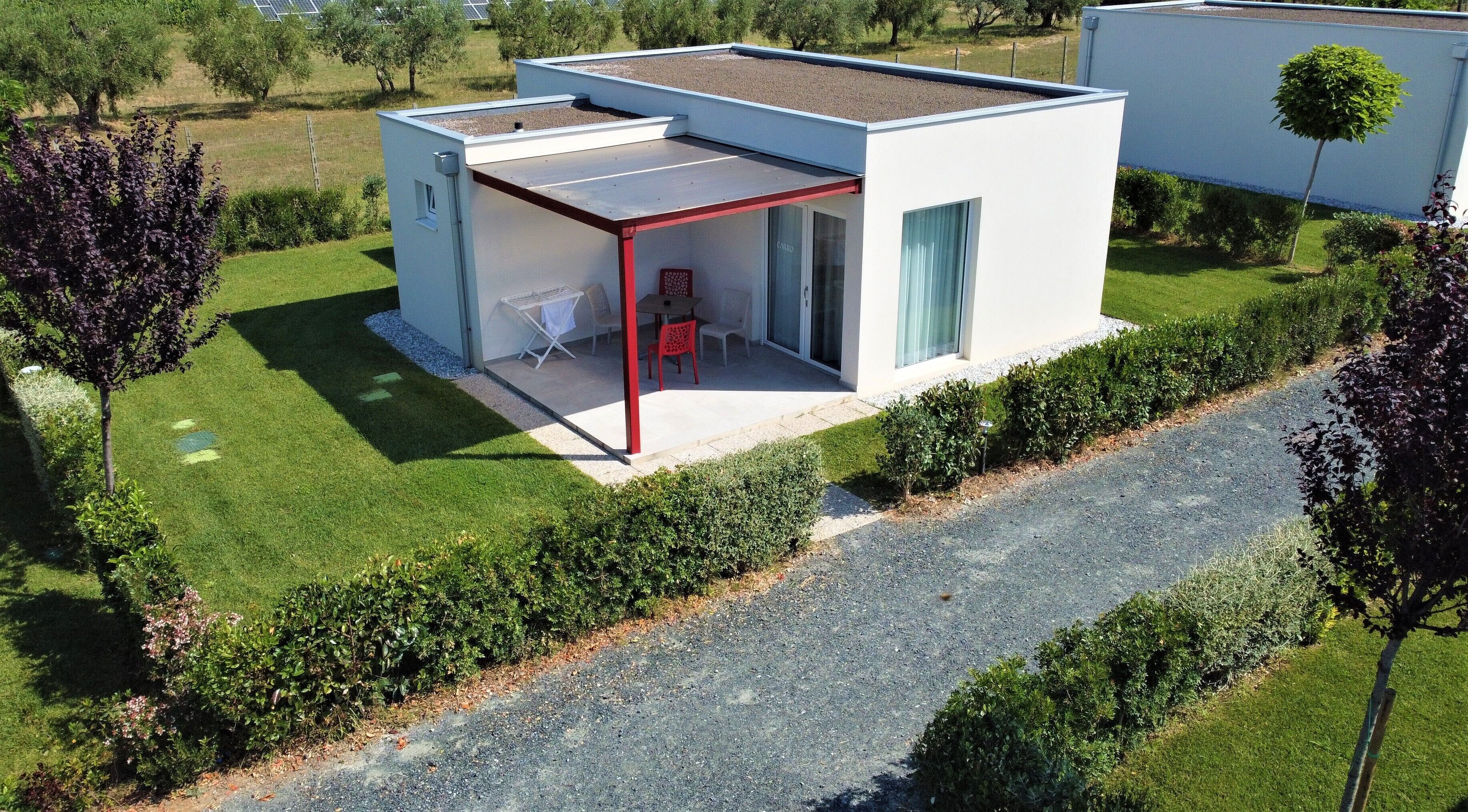 Una casa moderna de un piso con techo plano, un porche cubierto con mobiliario exterior y un jardín cuidado.