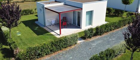 Una casa moderna de un piso con techo plano, un porche cubierto con mobiliario exterior y un jardín cuidado.