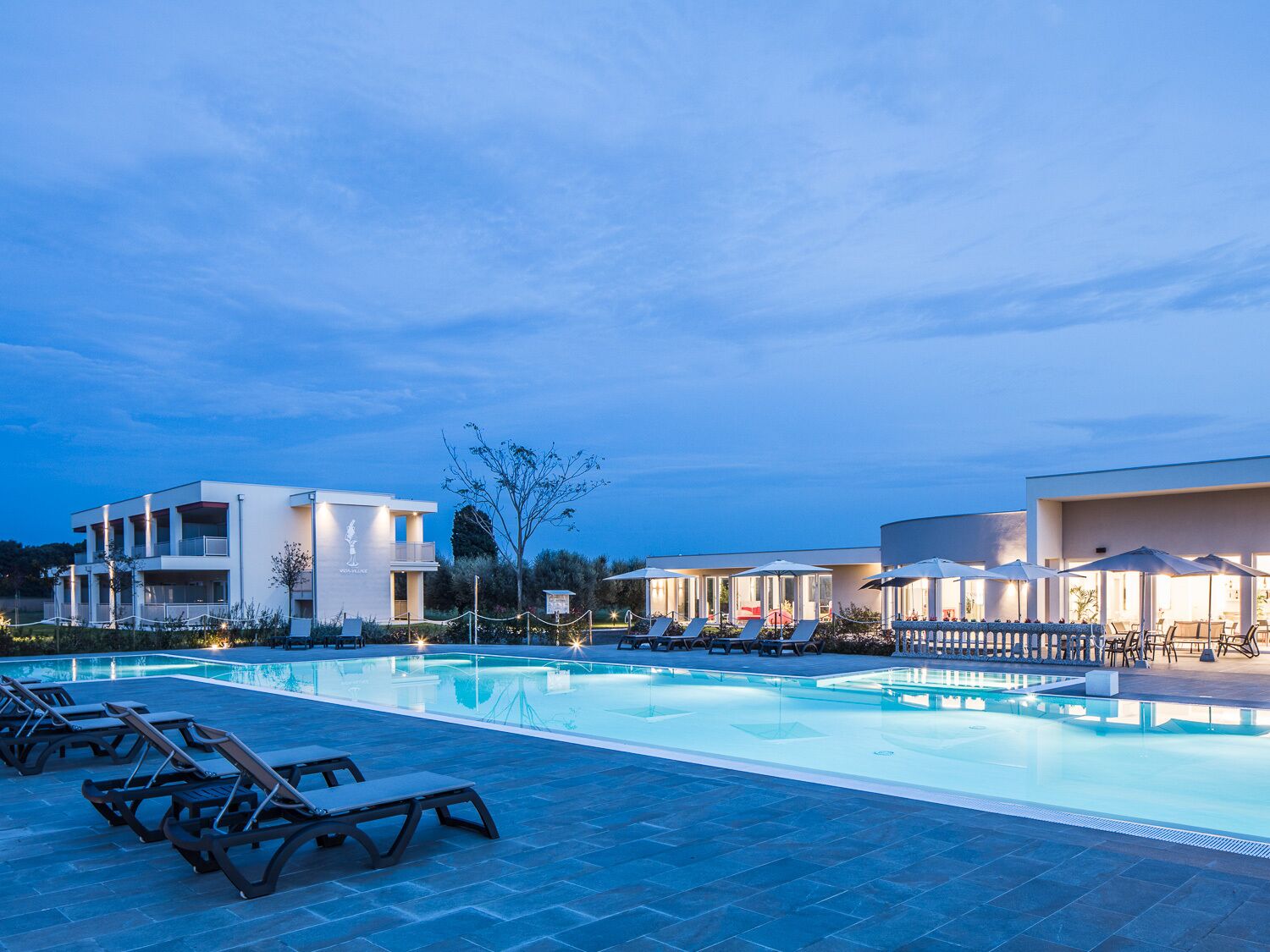 A swimming pool with lounge chairs and umbrellas, surrounded by modern buildings with balconies.