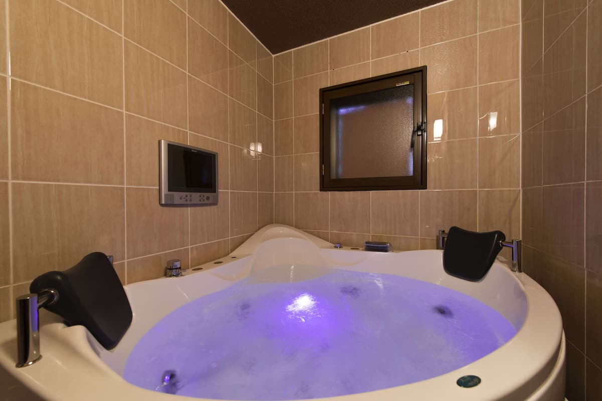Un baño con una bañera grande, un espejo y una pequeña pantalla.