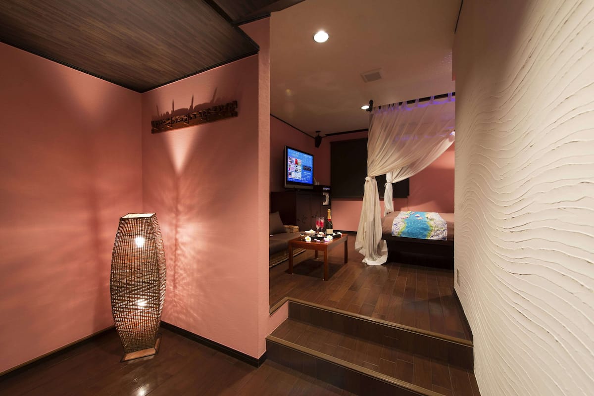 Habitación de hotel con un jarrón grande, un televisor, una cama con dosel y una pequeña mesa con adornos.
