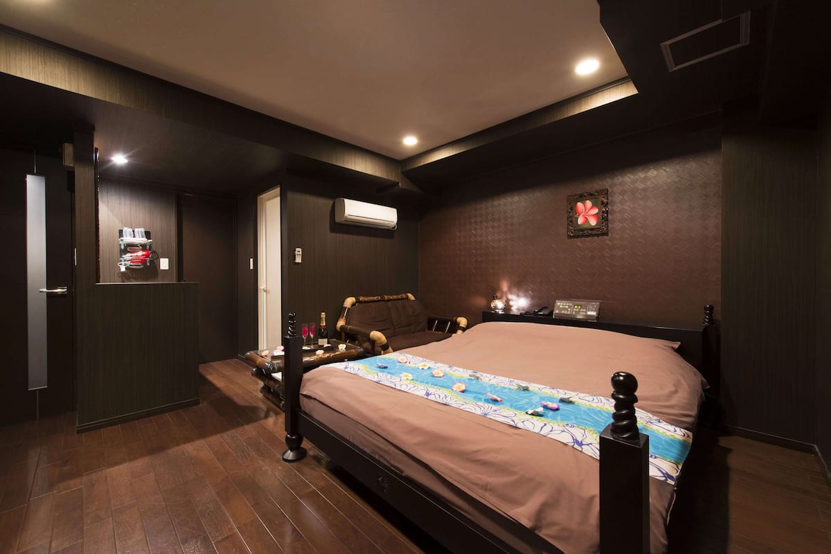 Habitación de hotel con una cama grande, una mesita de noche, un aire acondicionado y un estante pequeño con artículos de aseo.