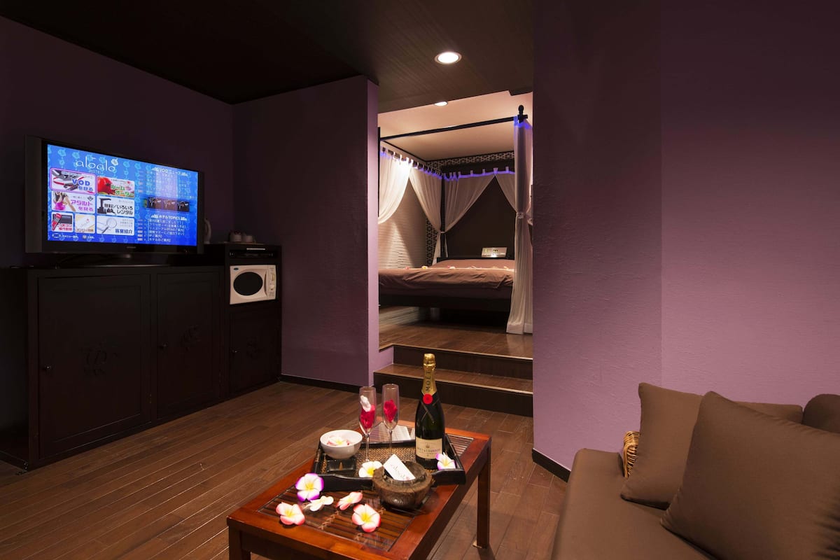 Una habitación con una cama, un televisor, una mesita de café con flores y una botella de champán.