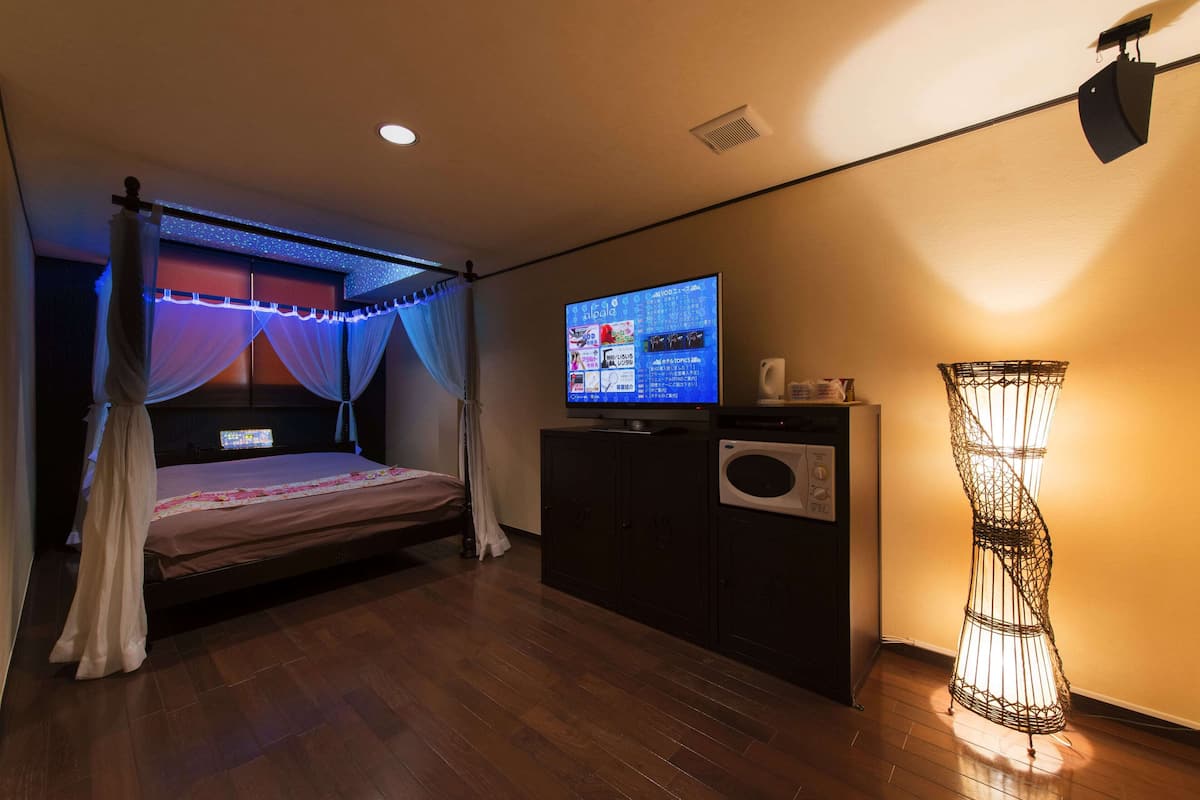 Un dormitorio con cama, televisor, armario y una lámpara de pie decorativa.