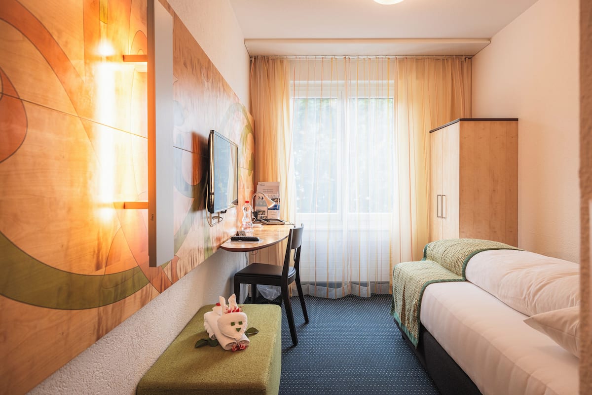 Ein Hotelzimmer mit einem Bett, einem Schreibtisch, einem Sessel, einem Fernseher und einem Fenster mit Vorhängen.