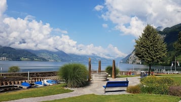 A lakeside view with a dock, boats, a bench, and a mountain backdrop.