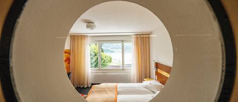 A hotel room with a bed, a window with curtains, and a view of greenery outside.