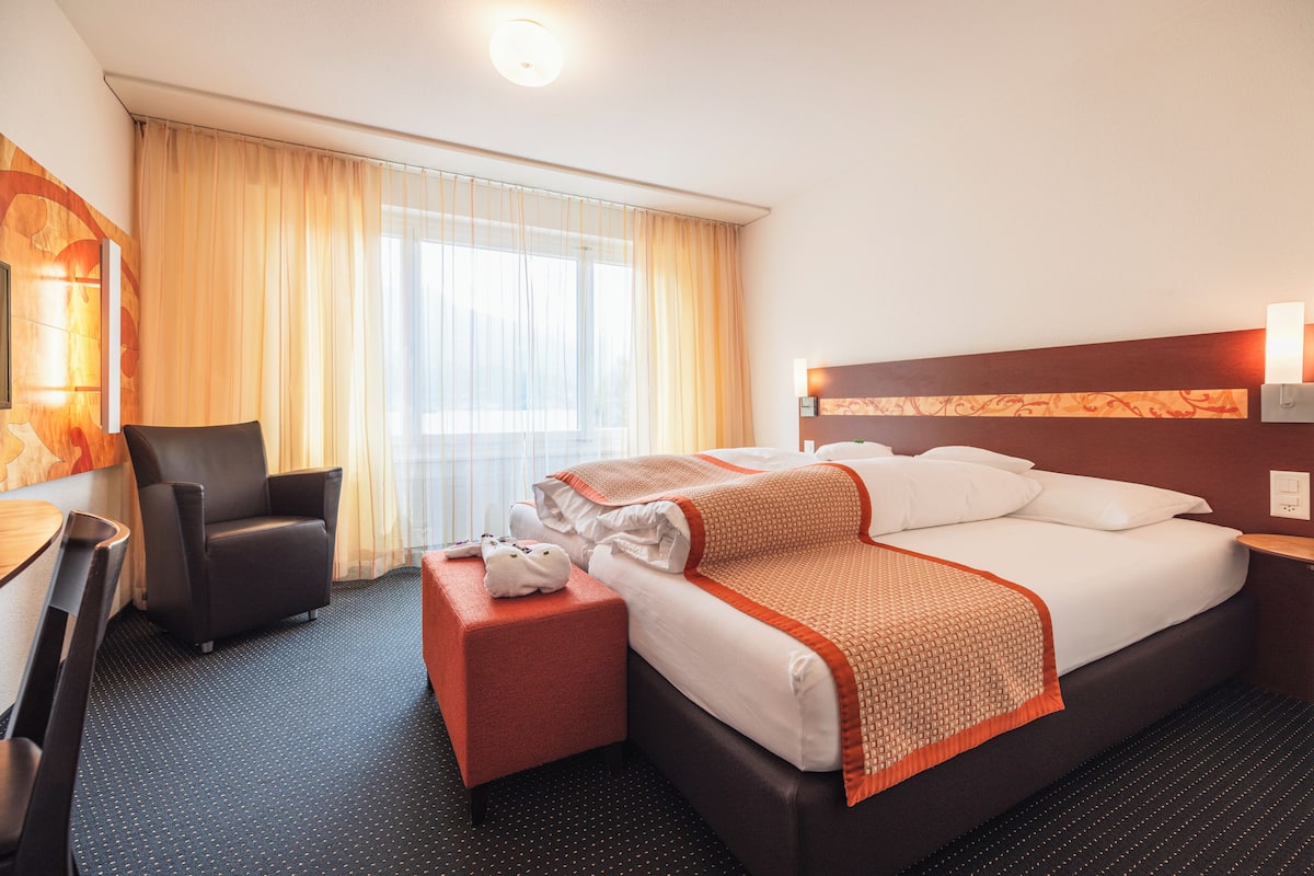 Ein Hotelzimmer mit Bett, Stuhl, Schreibtisch und einem Fenster mit Vorhängen.