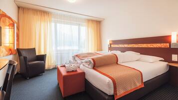Una habitación de hotel con cama, una silla, un escritorio y una ventana con cortinas.