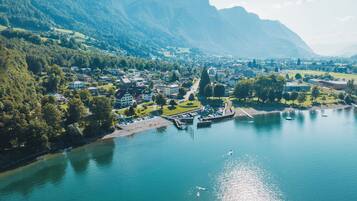 An aerial view of a lakeside town with residential buildings, a marina, and a mountain backdrop.
