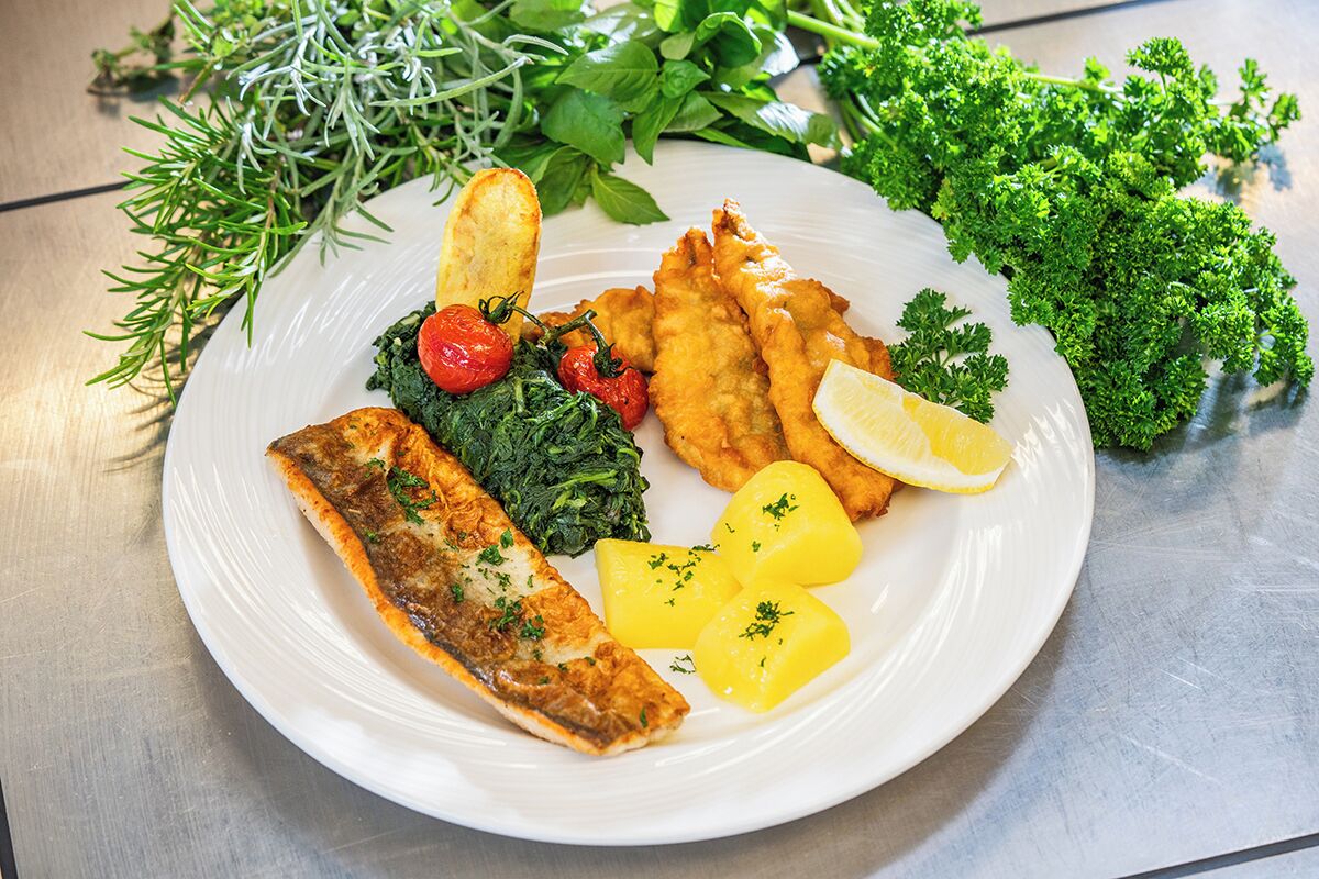 Un plato de comida con pescado, patatas y verduras de hoja verde.