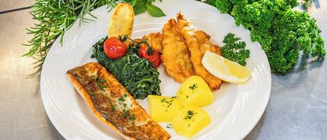 Une assiette de nourriture comprenant du poisson, des pommes de terre et des légumes verts.