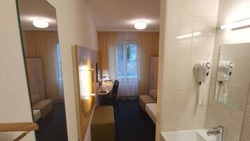A hotel room with a bathroom, a bed, a desk, and a chair.